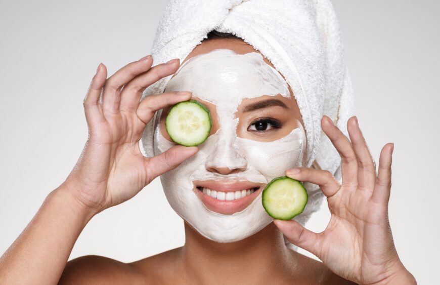 Attractive smiling lady with scrab on face holding cucumber slices isolated
